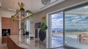 Une cuisine moderne dotée d’un îlot central aux lignes courbes, de grandes fenêtres et offrant une vue sur un paysage.