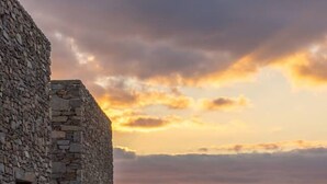 Un bâtiment en pierre doté d’une terrasse, de sièges en plein air et offrant une vue sur la mer au coucher du soleil.