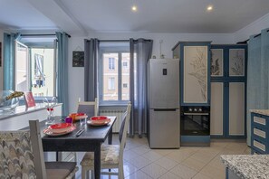 A modern kitchen with a refrigerator, oven, and dining area with a table set for two. - Sweet Coccagna by Wonderful Italy (Genoa)