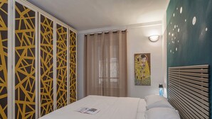 Quarto de hotel com cama, luminária na parede, pintura e divisória decorativa com padrões geométricos.