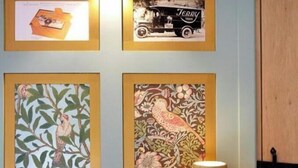 A room with a bed, a lamp, and four framed artworks on the wall.