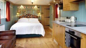 A cozy room with a bed, wooden cabinets, a kitchen area, and a ceiling light fixture.