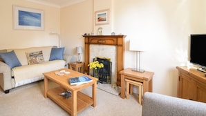 A living room with a fireplace, a sofa, a coffee table, a television, and a small table with a lamp. - Mead Cottage (Bridport)
