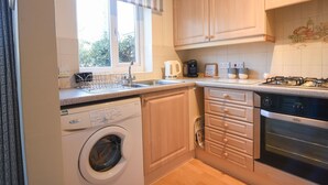 A compact kitchen with a washing machine, a coffee maker, and a gas stove. - Mead Cottage (Bridport)