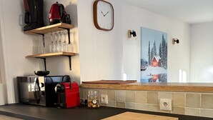 Keittiössä on puiset kaapit, musta työtaso, kello ja taulu, jossa on lumisen mökin kuva.