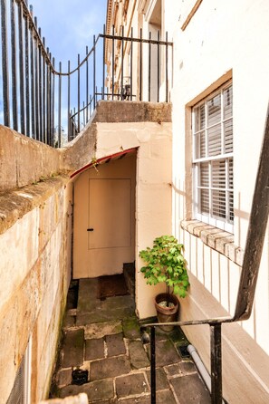 A narrow alleyway with a potted plant, a door, and a window with shutters. - Parade Watch (Bath)