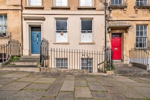 A building with a blue door, a red door, and a window with a wreath. - Parade Watch (Bath)