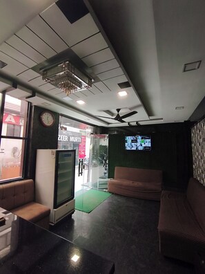 A hotel lobby with a reception desk, seating area, and a television screen displaying a menu.