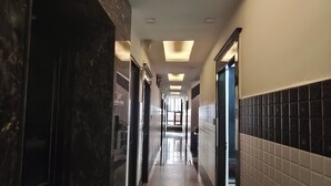A corridor with a marble floor, recessed lighting, and a view into a room with a bed and a window. - Hotel Gulmohar  (Haridwar)