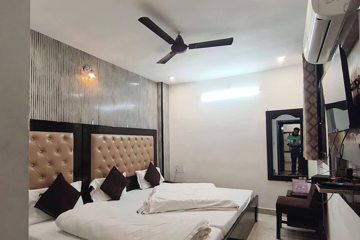 A hotel room with a bed, a desk, an air conditioner, a ceiling fan, and a mirror.