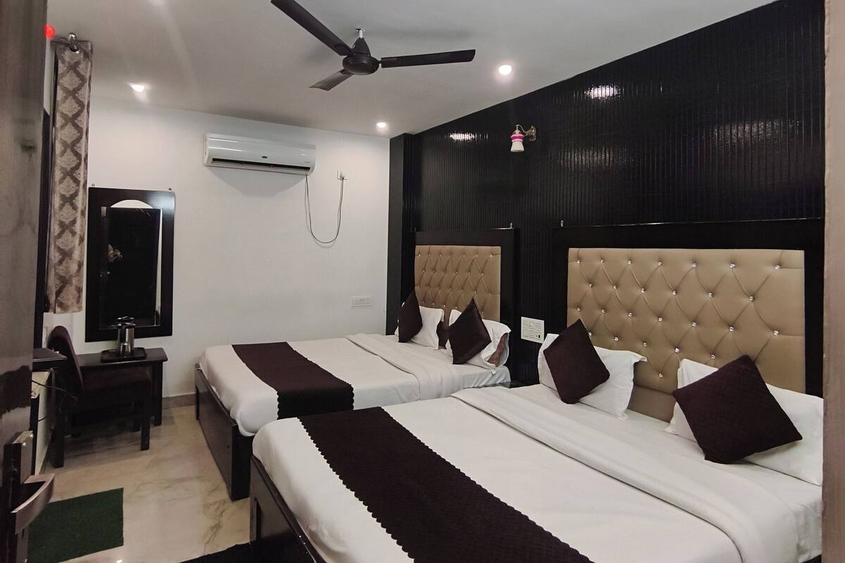 A hotel room with two beds, a desk, a chair, a ceiling fan, and an air conditioning unit.
