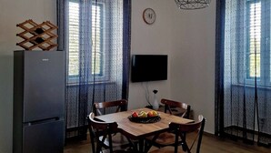 A dining area with a wooden table, four chairs, a refrigerator, a flat-screen TV, and a clock on the wall. - Welcoming 1-bedroom villa with AC in Radovići (Radovići)