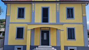 A two-story building with a yellow facade and blue window frames, featuring a central entrance with steps leading up to it. - Welcoming 1-bedroom villa with AC in Radovići (Radovići)