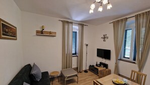 A living room with a sofa, a dining table, a TV, and a ceiling light fixture. - Welcoming 1-bedroom villa with AC in Radovići (Radovići)
