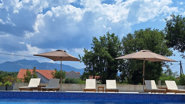 A swimming pool with lounge chairs and umbrellas, surrounded by a tiled deck and a view of mountains. - Welcoming 1-bedroom villa with AC in Radovići (Radovići)