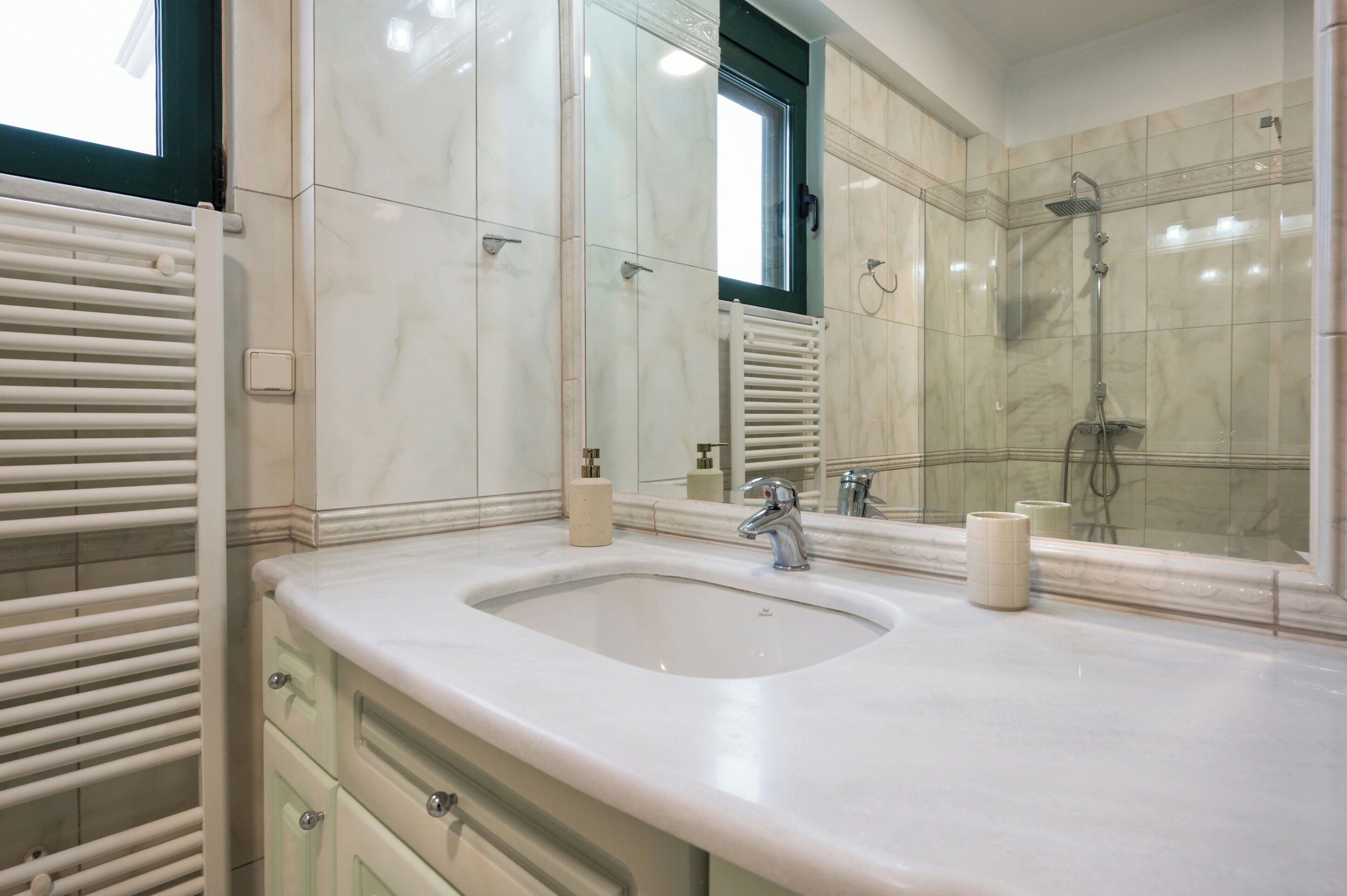 Un baño con lavamanos, espejo, ducha y armarios.