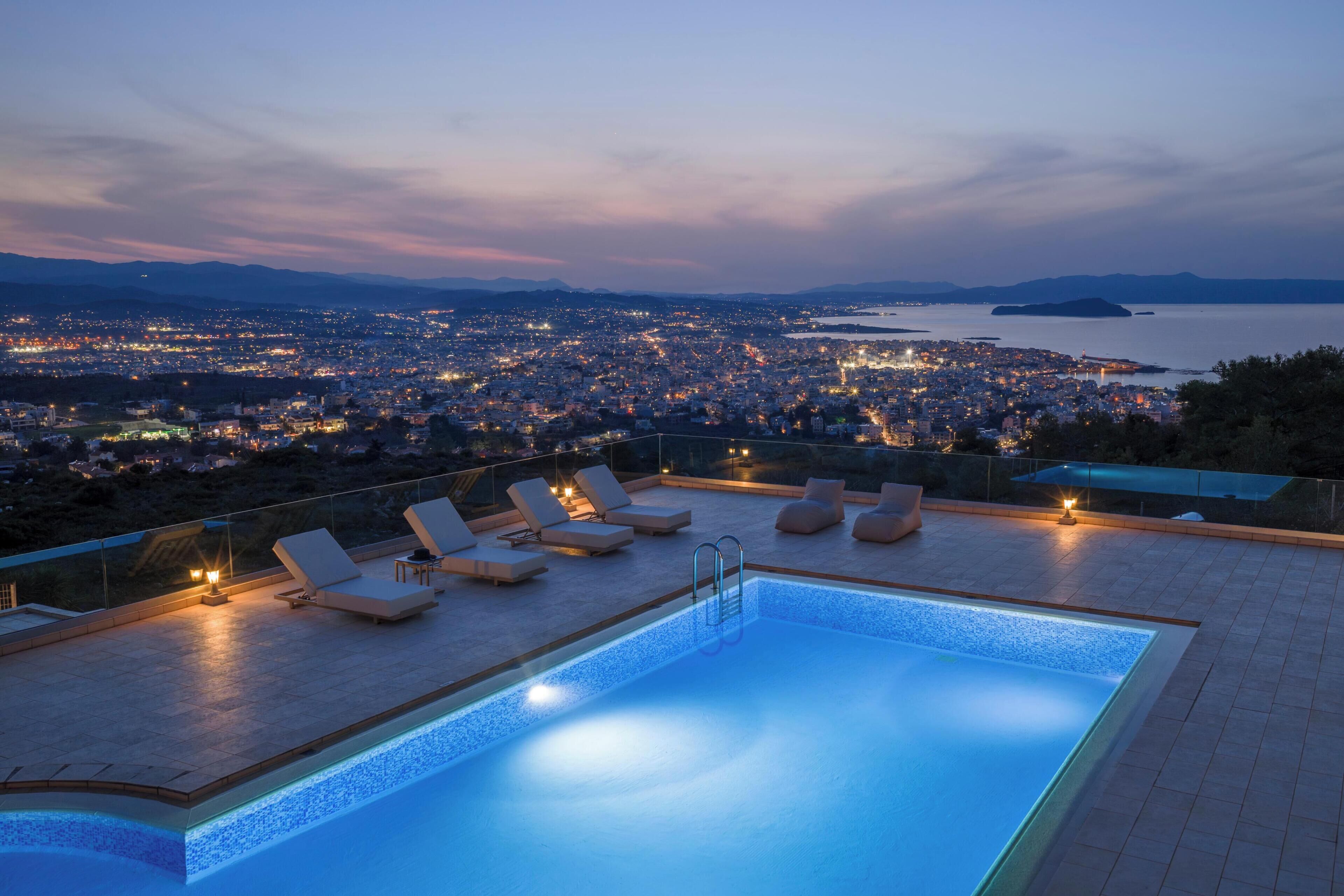 A rooftop pool with lounge chairs and a view of a cityscape at dusk.