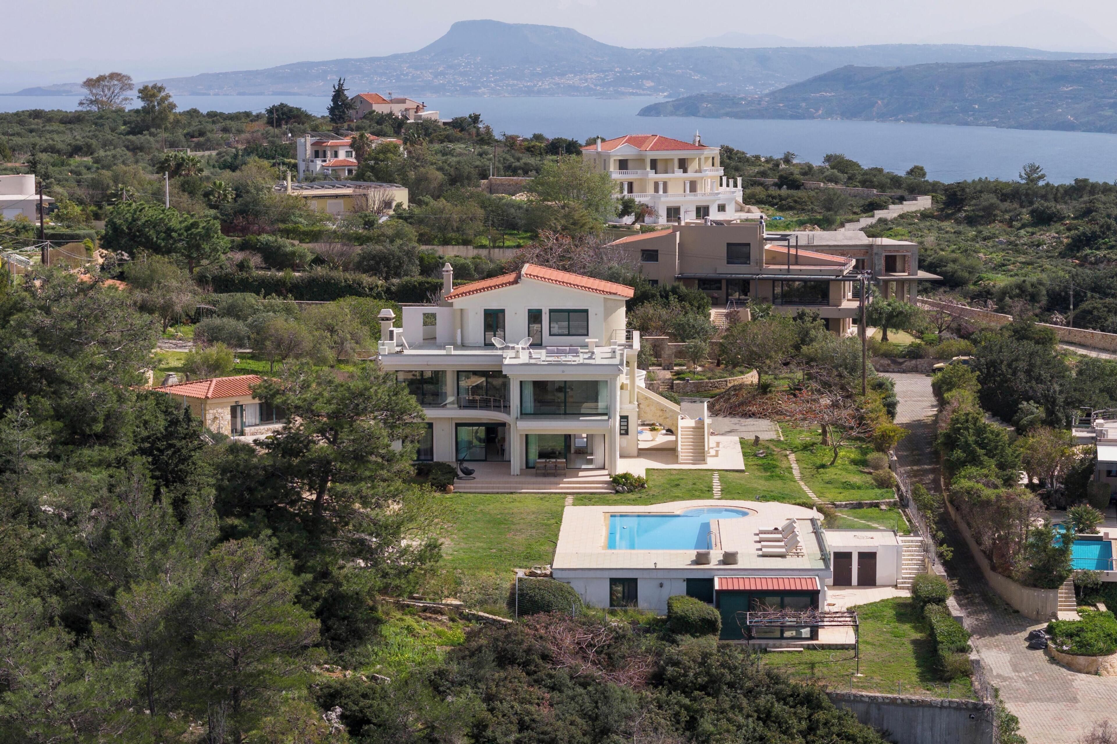 Une villa moderne dotée d’une piscine, entourée d’une végétation luxuriante et offrant une vue sur un plan d’eau.