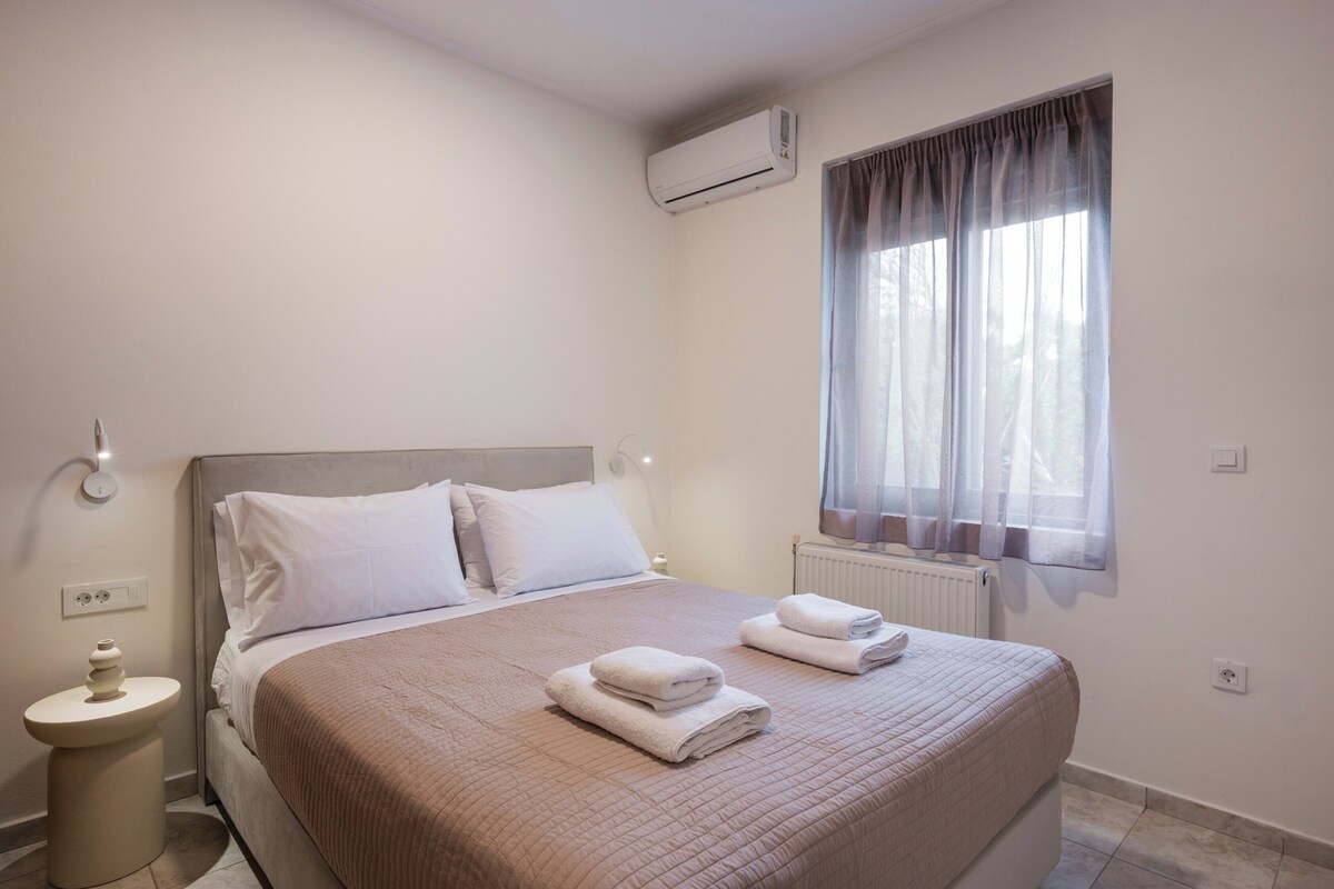 A bedroom with a bed, two bedside tables, an air conditioner, a window with curtains, and a radiator.
