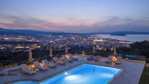 A rooftop pool with lounge chairs and umbrellas, overlooking a cityscape at dusk. - Lithea Estate Collection (Chania)