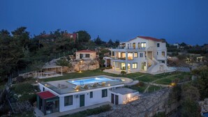 A modern two-story house with a swimming pool, a covered patio, and a stone retaining wall. - Lithea Estate Collection (Chania)
