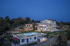 Ein modernes, zweistöckiges Haus mit Schwimmbad, überdachter Terrasse und einer Steinmauer.