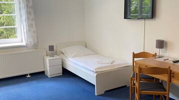 Een slaapkamer met een bed, een bureau, een stoel, een televisie en een raam met gordijnen.