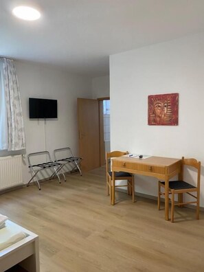 Ein Zimmer mit einem Holztisch, zwei Stühlen, einem an der Wand befestigten Fernseher und einer Tür zu einem anderen Raum.