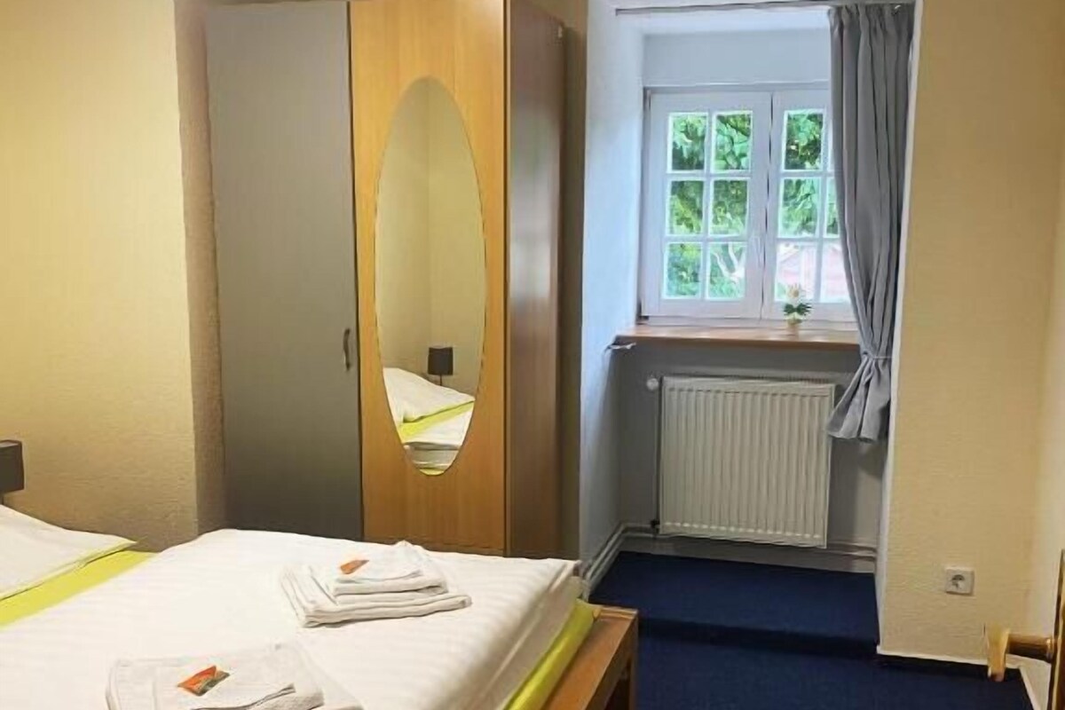 Una habitación de hotel con cama, armario, ventana con cortinas y radiador.