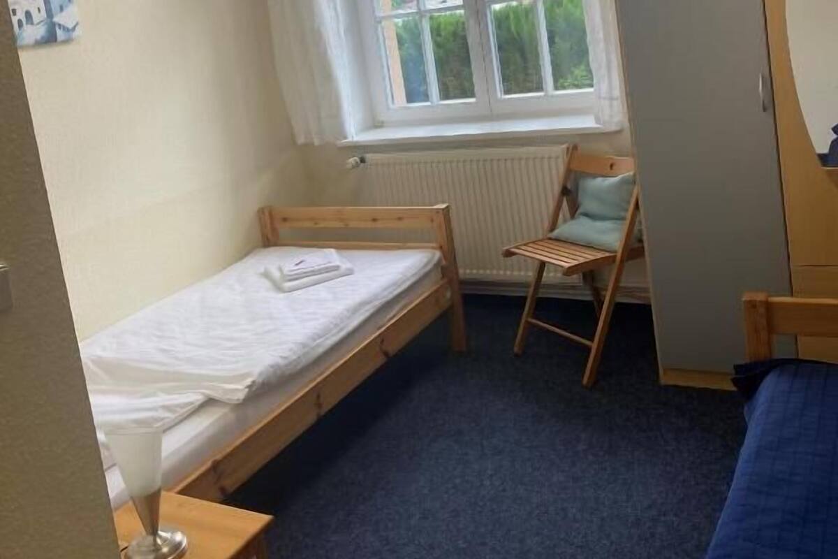 A small room with a single bed, a chair, a radiator, and a window with curtains.