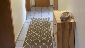 A hallway with a patterned rug, wooden doors, and a small wooden cabinet with a basket.
