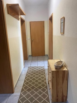 A hallway with a patterned rug, wooden doors, and a small wooden cabinet with a basket. - VITA Ferienresidenz (Neu Kaliß)