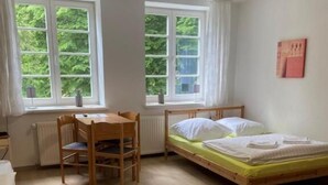 A room with a bed, a wooden table, and two windows with curtains.