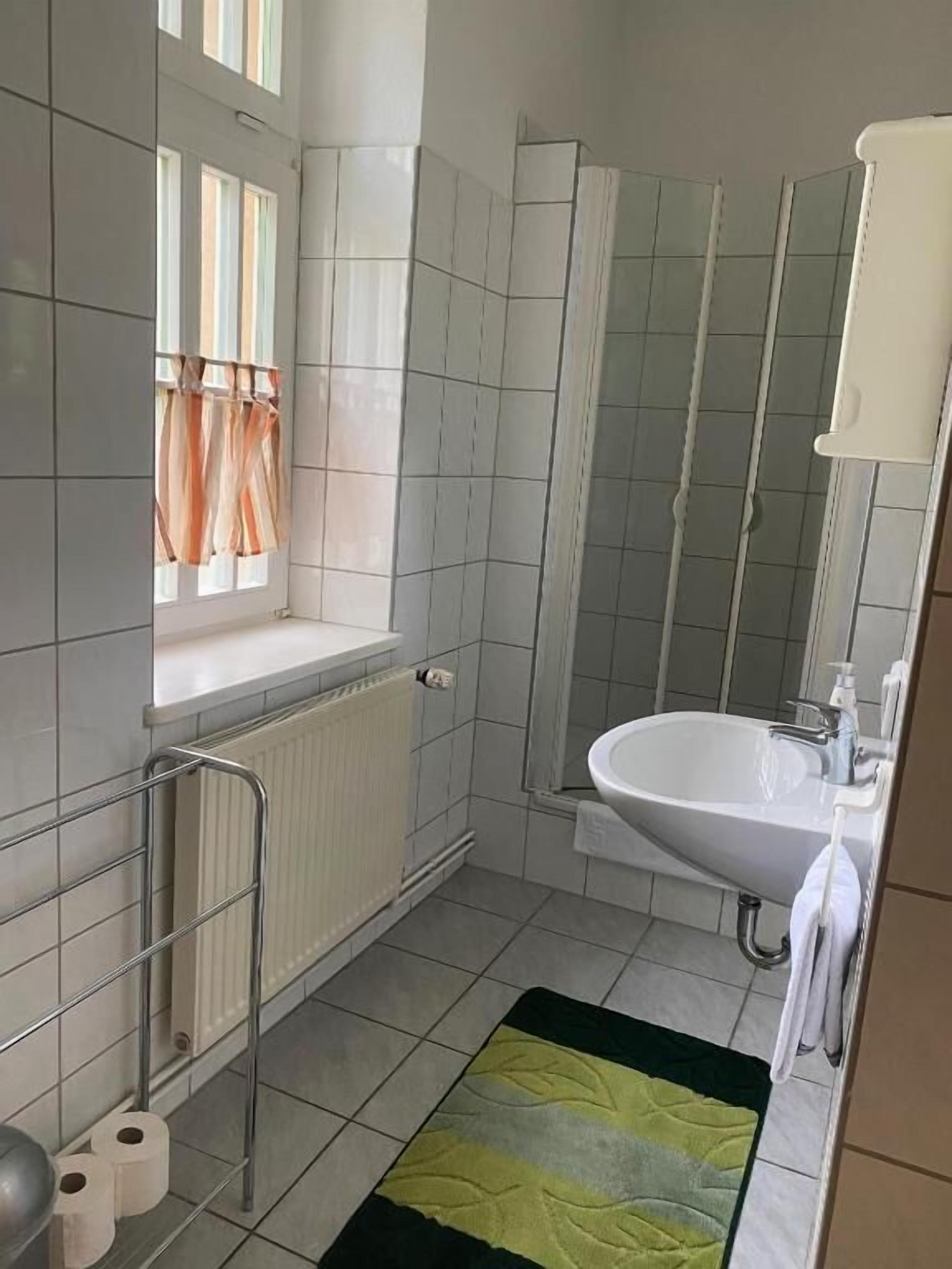 A bathroom with a window, a radiator, a sink, and a shower.