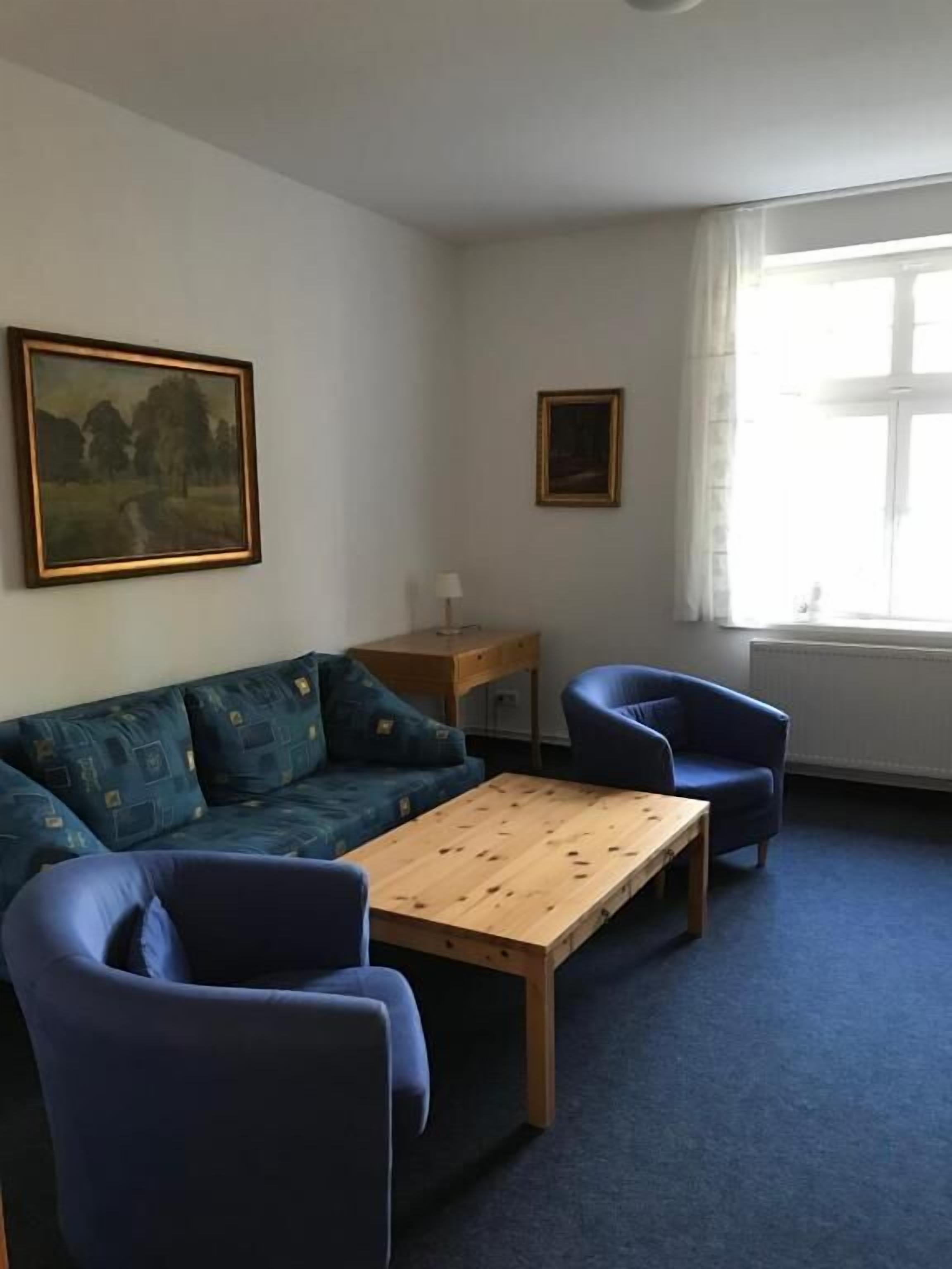 A room with a sofa, two chairs, a wooden table, a painting, and a window.