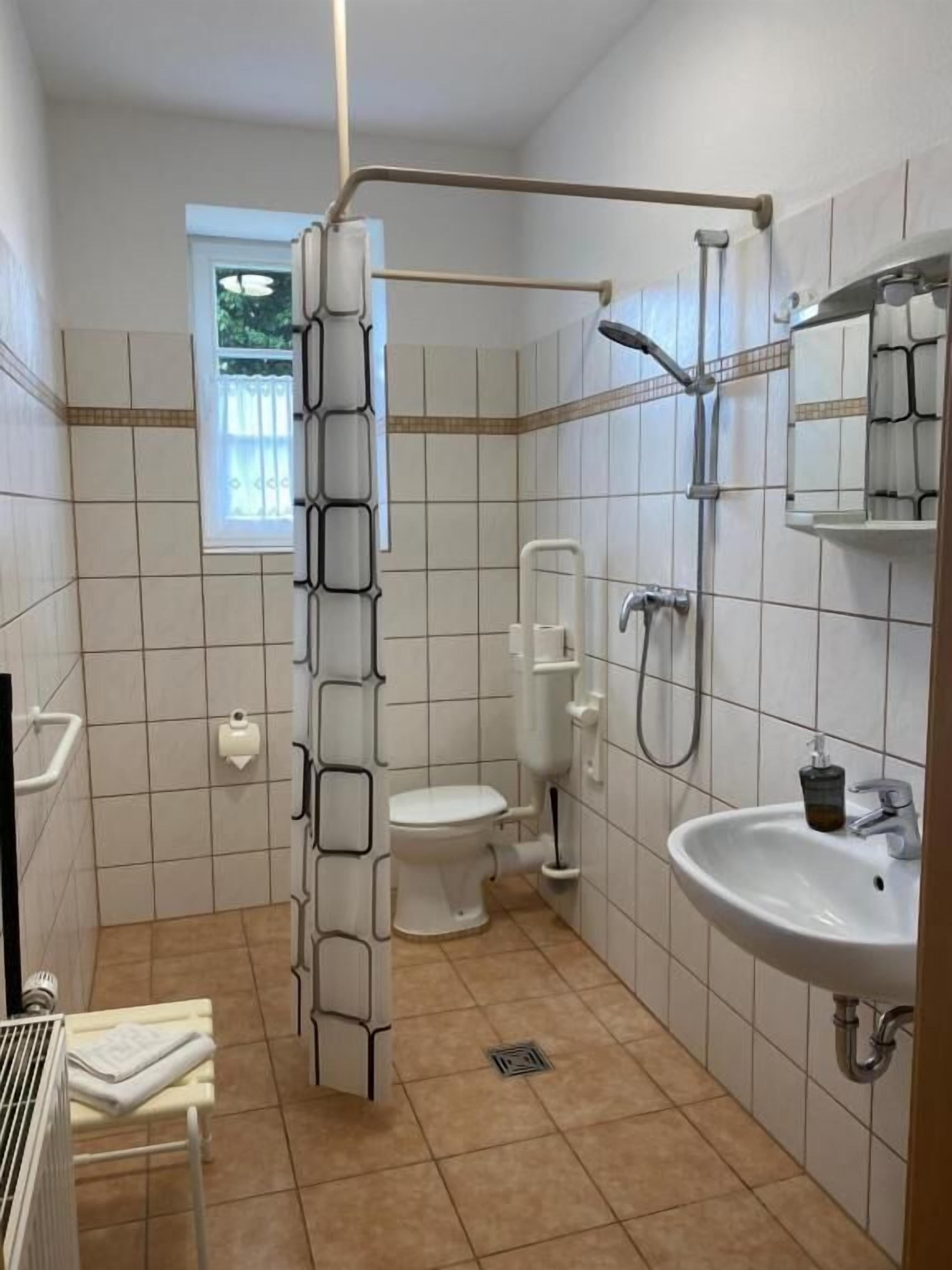 A bathroom with white tiles, a toilet, a shower, a sink, and a towel rack.