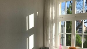 A room with a wooden table and chairs, a window with curtains, and a view of greenery outside.