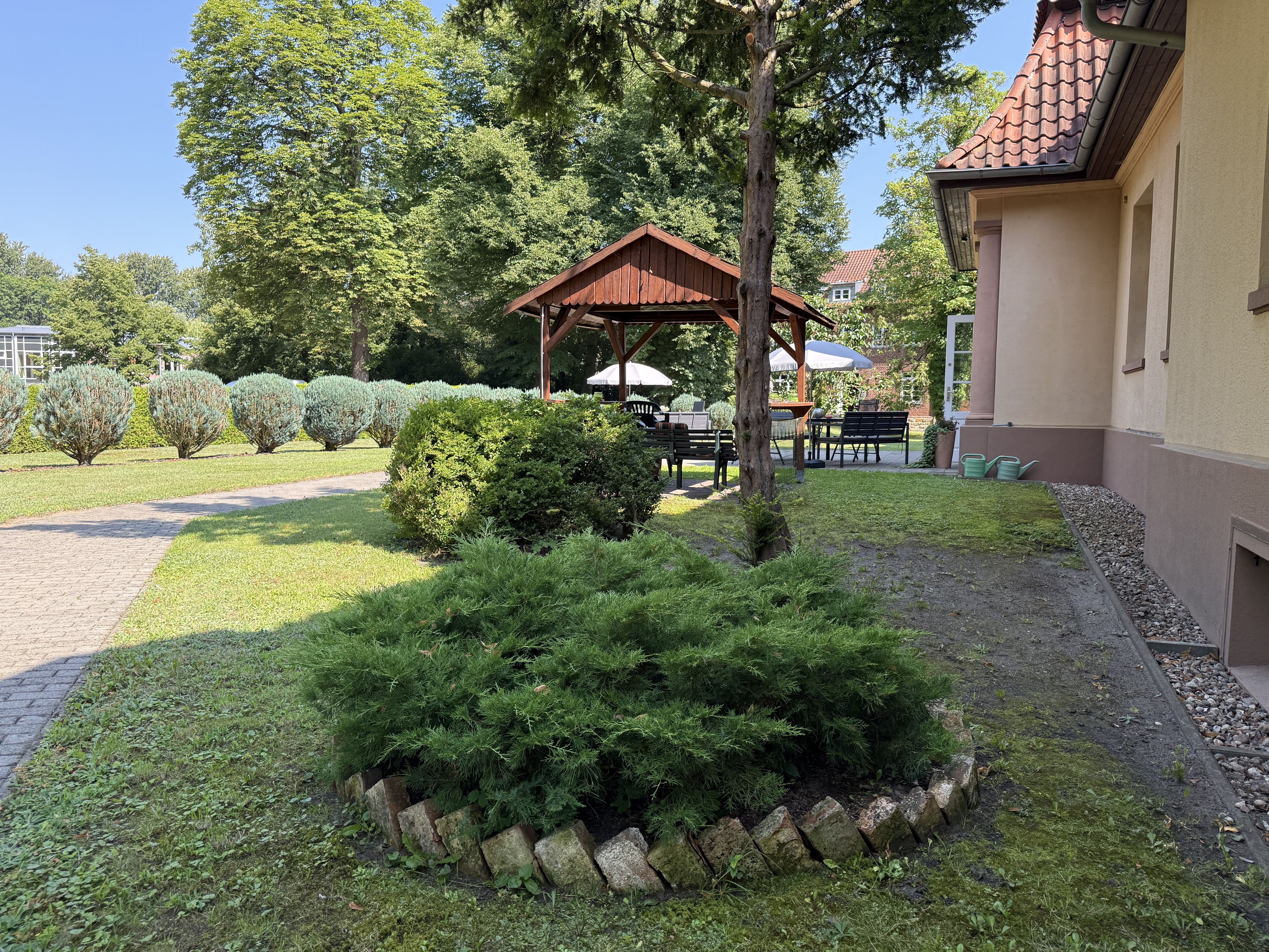 A garden with a gazebo, a lawn, and a building with a tiled roof.