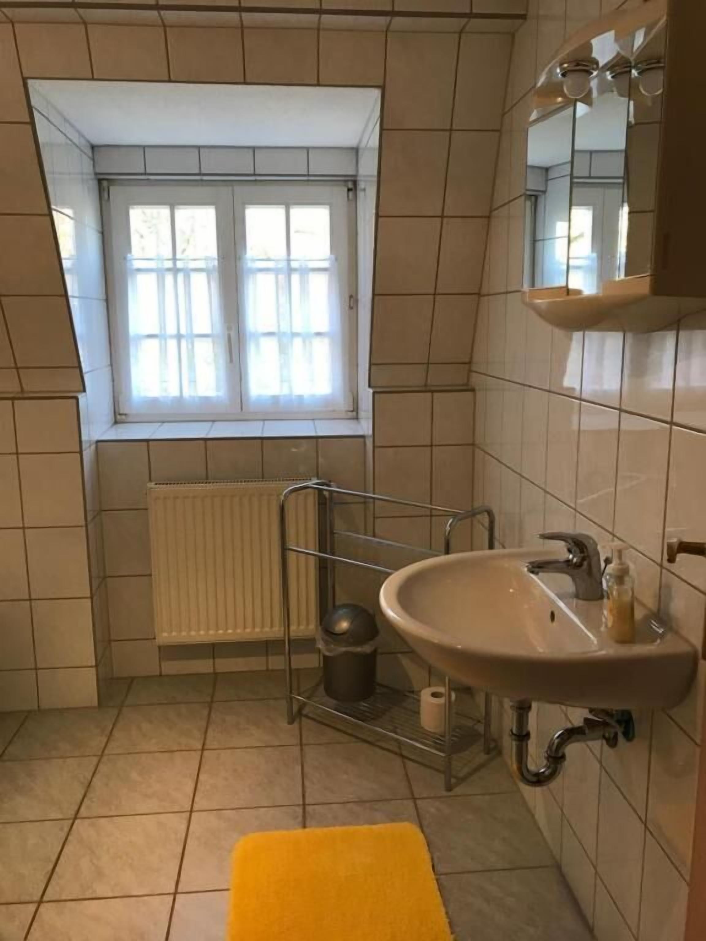 A small bathroom with a window, a radiator, a sink, and a yellow rug.