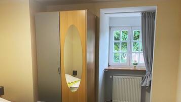 A hotel room with a bed, a mirror, a window with curtains, and a radiator.