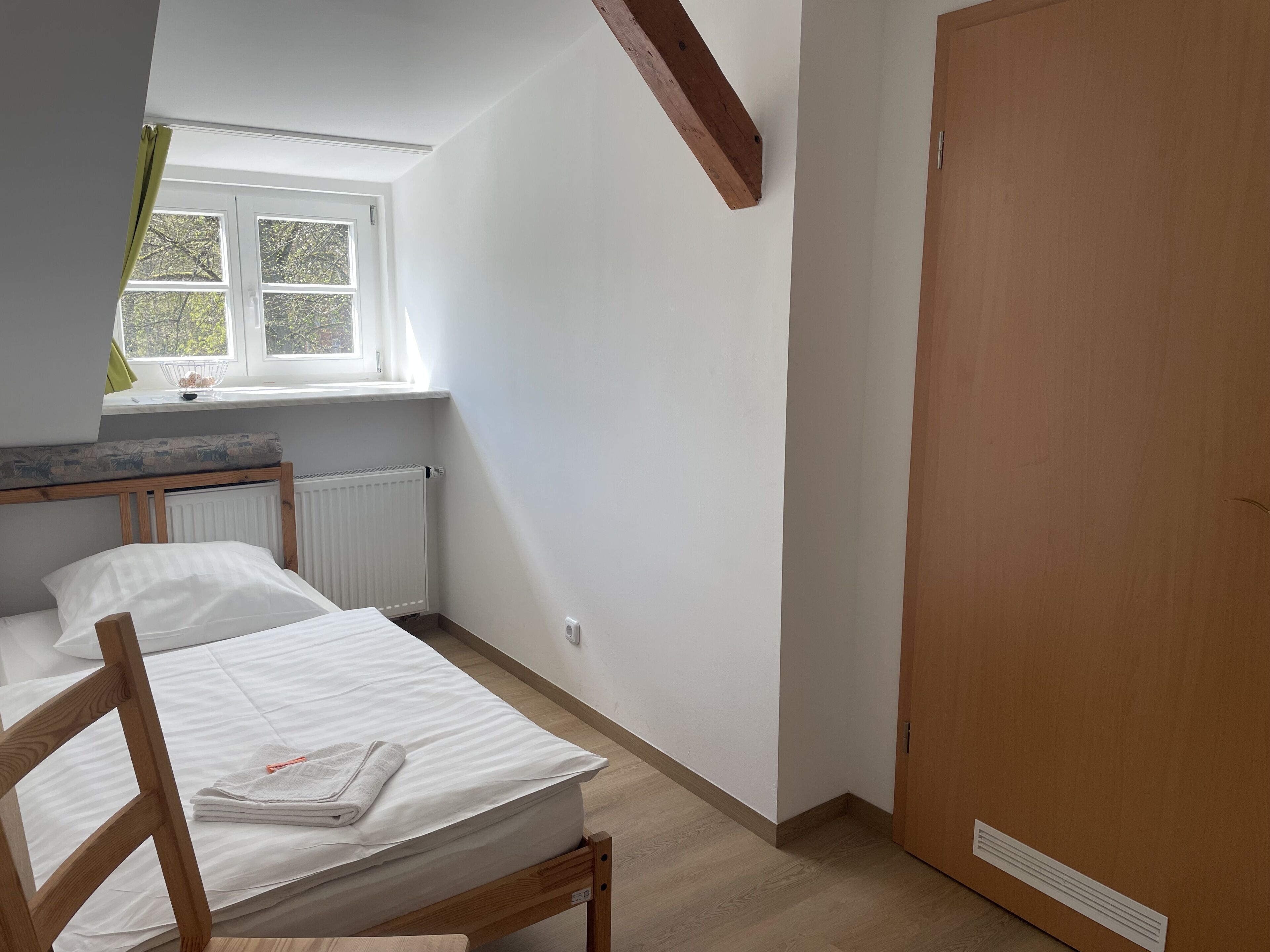 A bedroom with two beds, a window, a radiator, and a wooden door.
