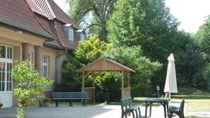 A building with a red-tiled roof, a wooden gazebo, outdoor seating, and a lawn.
