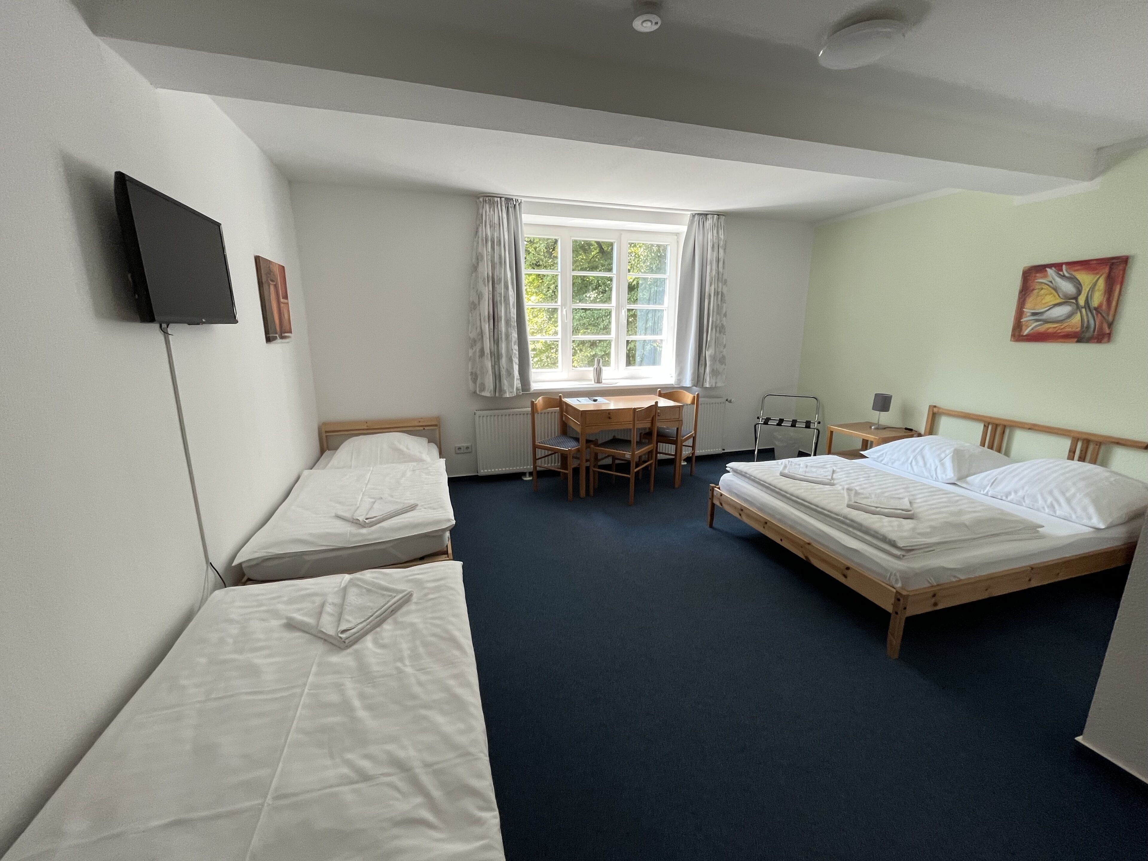 Ett hotellrum med två separata sängar, ett skrivbord med en stol, ett element, ett fönster med gardiner och en tavla på väggen.