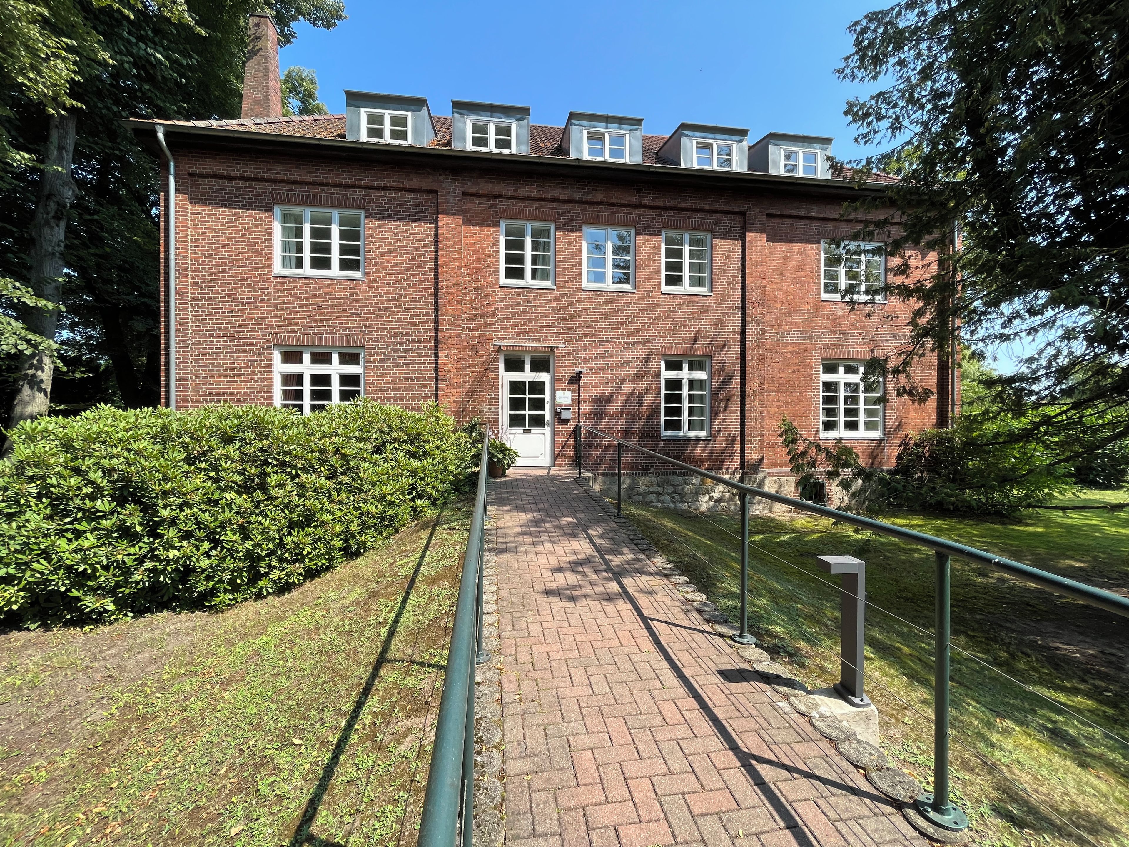 A brick building with multiple windows and a paved pathway leading to the entrance.