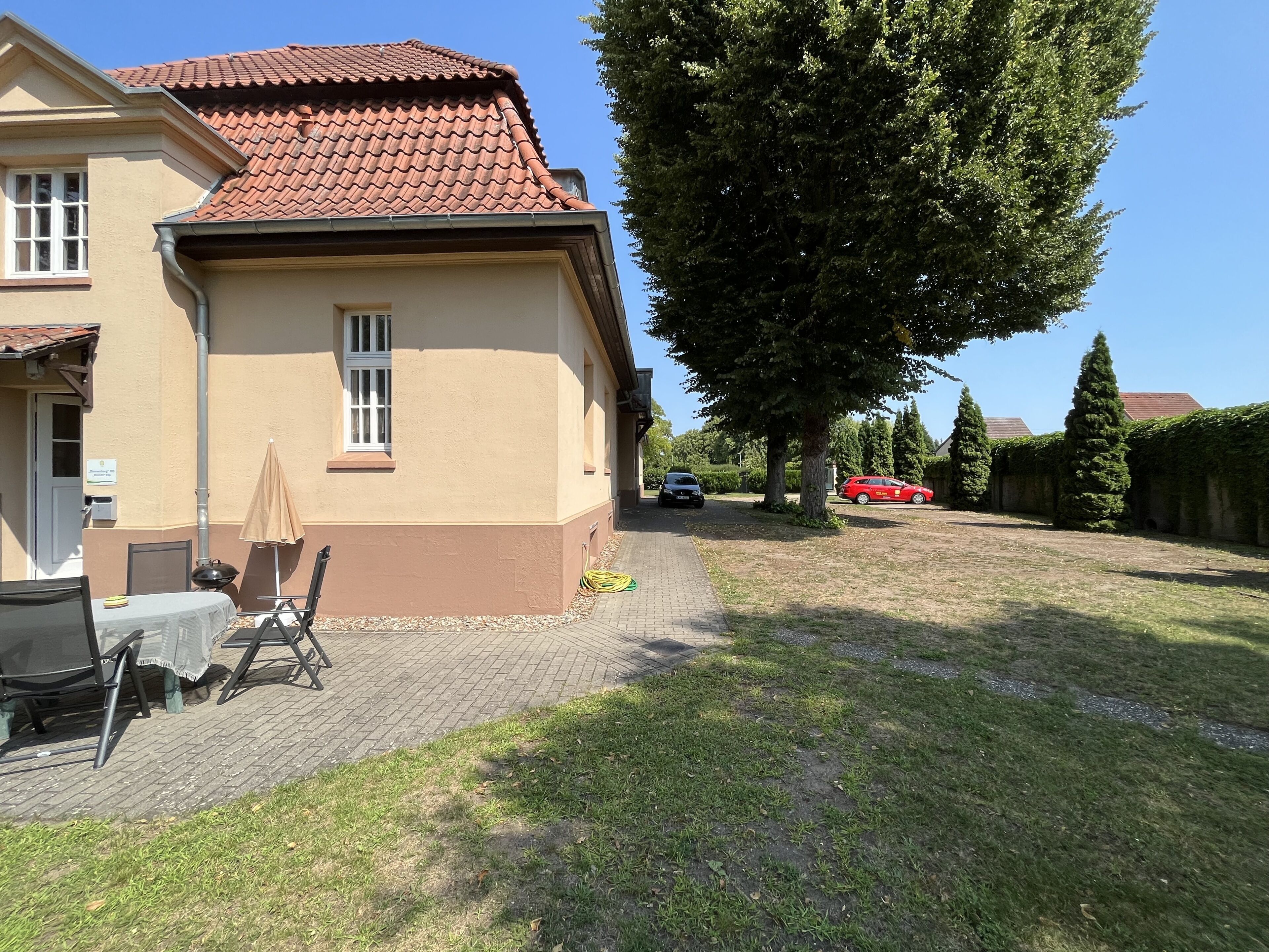 A house with a tiled roof, a paved patio with outdoor furniture, and a large tree in the yard.