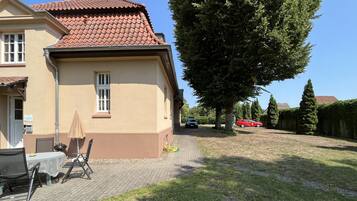 A house with a tiled roof, a paved patio with outdoor furniture, and a large tree in the yard.