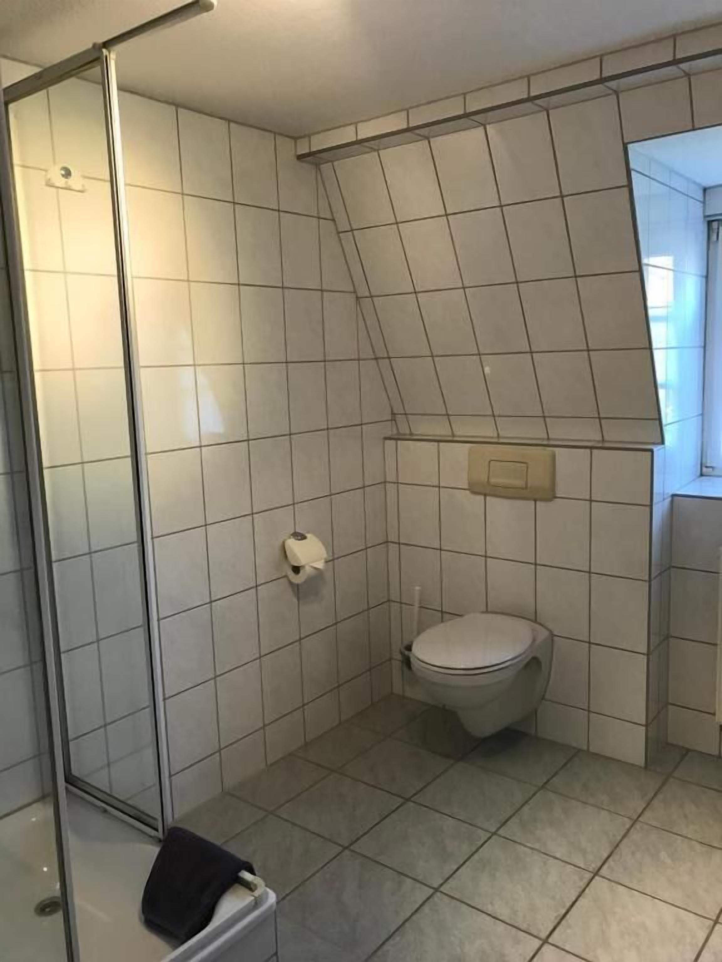 A small, tiled bathroom with a shower, toilet, and a towel rack.