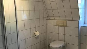A small, tiled bathroom with a shower, toilet, and a towel rack.