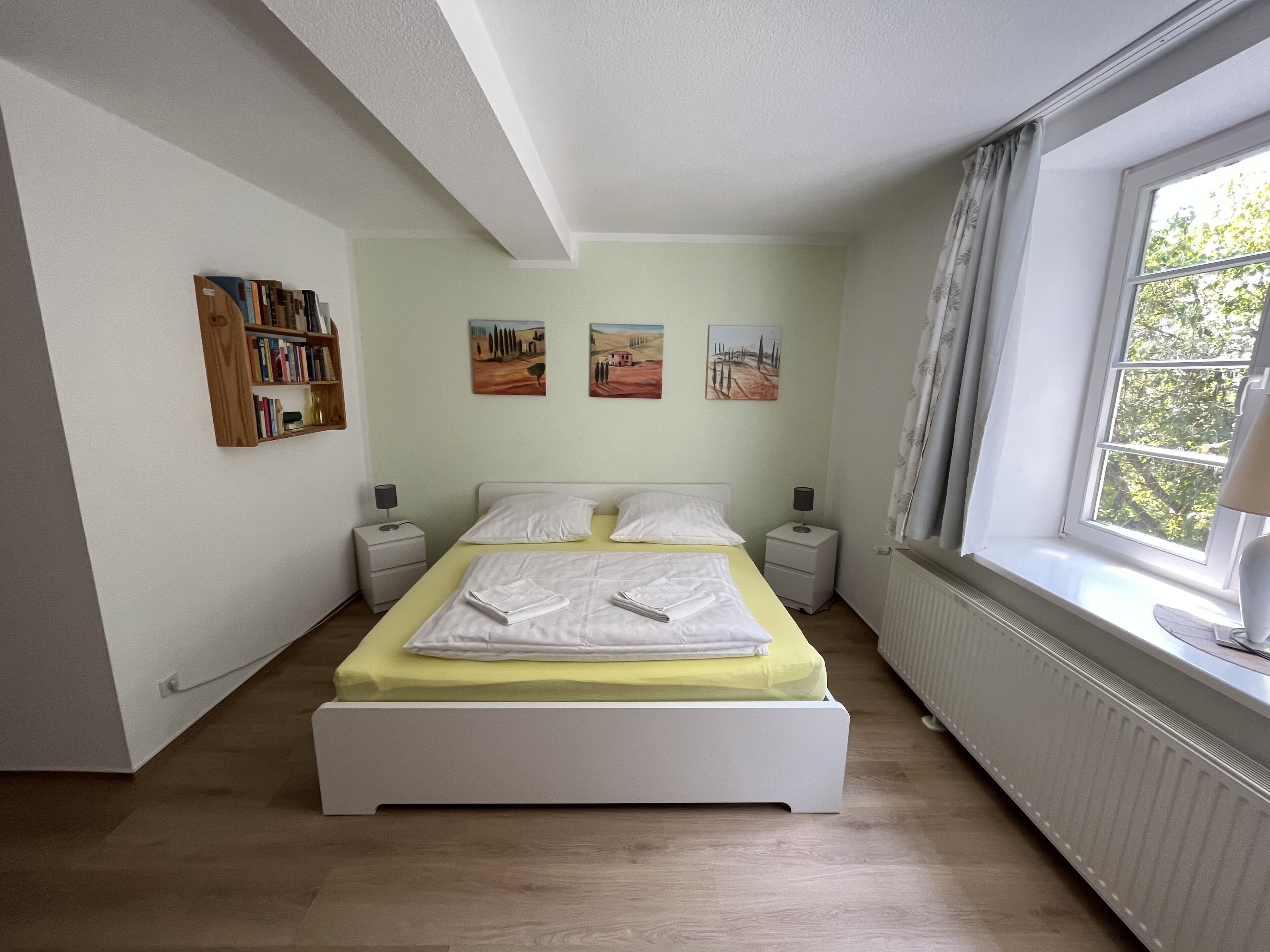 Una camera da letto con un letto, comodini, un termosifone e una finestra con tende.