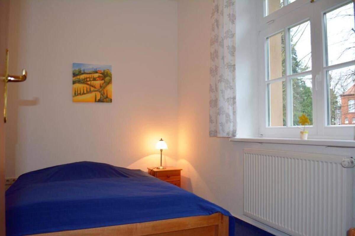 A bedroom with a bed, a nightstand with a lamp, a window with curtains, and a wall painting.